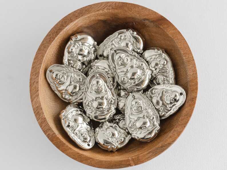 Buddha pendants made from silver tone metallic finish plastic. Size 32x22mm with a 1mm hole for a jump ring at the top. These   shiny silver pendants have  a sitting buddha design on from and back.