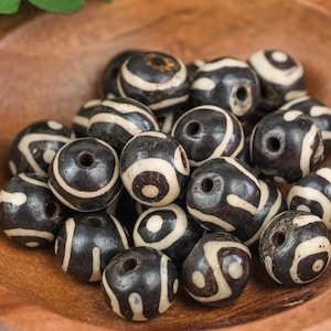 May include: A bowl of black and white striped beads. The beads are made of bone and have a natural, rustic look.