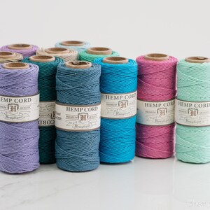 May include: Assortment of 10 spools of hemp cord in various colors, including lavender, teal, turquoise, pink, and mint green. Each spool has a label that reads "Hemp Cord" with a logo and the text "Premium Quality".