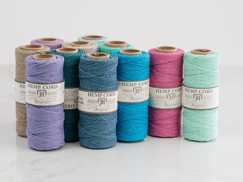 May include: Assortment of 10 spools of hemp cord in various colors, including lavender, teal, turquoise, pink, and mint green. Each spool has a label that reads "Hemp Cord" with a logo and the text "Premium Quality".