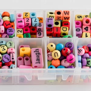 Puede incluir: Una caja de almacenamiento de pl&aacute;stico transparente con 10 compartimentos llenos de cuentas de letras de colores. Las cuentas son de varios colores, incluyendo rojo, azul, verde, amarillo y morado. Las cuentas est&aacute;n dispuestas en un patr&oacute;n aleatorio. La caja est&aacute; etiquetada con la palabra "laugh" en uno de los compartimentos.