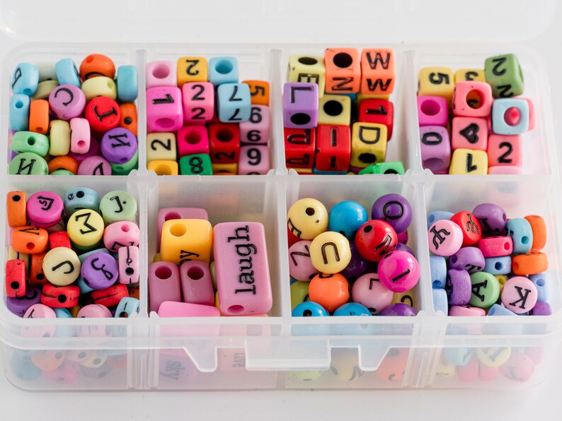 Puede incluir: Una caja de almacenamiento de pl&aacute;stico transparente con 10 compartimentos llenos de cuentas de letras de colores. Las cuentas son de varios colores, incluyendo rojo, azul, verde, amarillo y morado. Las cuentas est&aacute;n dispuestas en un patr&oacute;n aleatorio. La caja est&aacute; etiquetada con la palabra "laugh" en uno de los compartimentos.