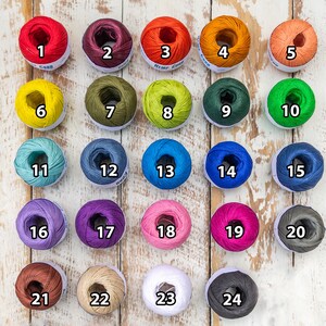 May include: Twenty-four balls of yarn in various colors, numbered 1 through 24. The yarn is wound into balls and arranged in rows on a white wooden surface.
