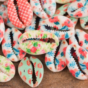 May include: A collection of white cowrie shells with various floral and checkered patterns in shades of red, pink, blue, and green.