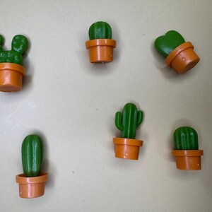 Könnte beinhalten: Sechs kleine Kakteen in Töpfen in verschiedenen Formen und Größen. Die Kakteen sind grün und die Töpfe sind orange.