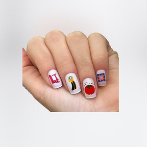 May include: Four fingernails with different designs. The first nail has a pink and white design with the letter "H". The second nail has a yellow and black design of a rotary cutter. The third nail has a red tomato with green leaves and a pincushion with needles. The fourth nail has a blue and orange patchwork design.