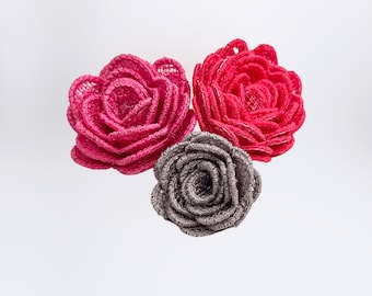 May include: Three fabric roses, one pink, one red, and one gray. The roses are layered and have a delicate, crocheted texture.
