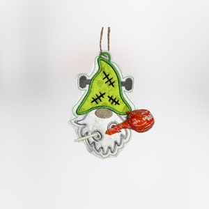 Peut inclure: Ornement de gnome sur le thème d'Halloween avec un chapeau vert de style Frankenstein et une barbe blanche. Le gnome a une sucette rouge attachée. L'ornement est en tissu et possède une ficelle pour l'accrocher.