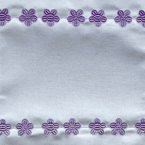 以下が含まれることがあります： 白い布地に、紫色の刺繍で花柄の縁取りが施されています。縁取りは、小さくシンプルな花柄のデザインで構成されています。