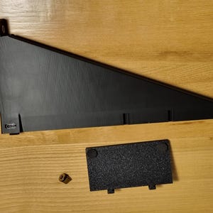 May include: Black, angled, electronic device stand with a rectangular base and a small, separate, textured black plate. A small, gold-colored screw is also present. The stand has a USB port.
