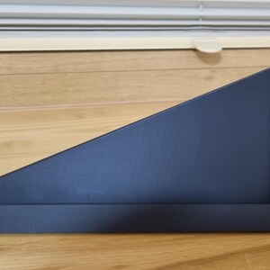 May include: A black, angled shelf with a rectangular base and a triangular top. The shelf is made of a matte material and has a small, square metal accent on the right side. The shelf is designed to be mounted on a wall.