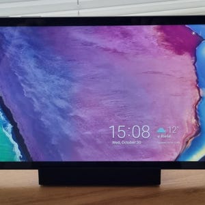 May include: A black tablet computer with a stand, displaying a purple and blue abstract background with a digital clock showing 15:08 and the date Wed, October 30. The weather forecast shows a cloudy icon and 12 degrees.
