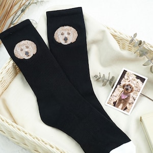 Könnte beinhalten: Schwarze gerippte Socken mit einer detaillierten Stickerei eines Hundegesichts. Die Socken haben weiße Zehen. Ein Foto eines Hundes mit einem rosa Bandana ist ebenfalls im Bild zu sehen.