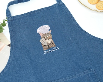 May include: A blue denim apron featuring an embroidered graphic of a brown tabby cat wearing a white chef hat and holding a silver spatula. The text "Gonzalito" is embroidered in white thread directly below the cat illustration on the chest.