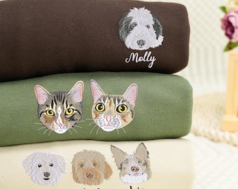 May include: Three stacked sweatshirts in dark brown, olive green, and cream. The brown sweatshirt features an embroidered dog face with the name Molly. The green one shows two cat faces. The cream sweatshirt displays three dog faces with the names Wiggles, Whiskey, and Leia.
