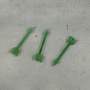 May include: Three green plastic arrows pointing in different directions. The arrows are on a light gray surface.