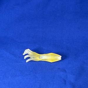 Op de afbeelding: Een doorschijnende gele plastic hand met vier vingers en een duim. De hand is gekruld in een grijpende positie.