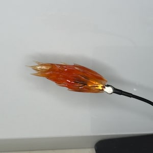 May include: A close-up of a red and orange flame-shaped object attached to a black cord. The object is made of a translucent material and appears to be a prop or decoration.