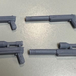 May include: Four gray plastic toy guns, two with scopes and two without. The guns are all in a similar style, with a barrel, a grip, and a trigger.