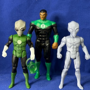 Puede incluir: Tres figuras de acción, dos son verdes y una es gris. Las figuras verdes son Green Lantern, una es humana y la otra es extraterrestre. La figura gris es un extraterrestre. El Green Lantern humano lleva un traje negro con una pieza de pecho verde y botas verdes. El Green Lantern extraterrestre lleva un traje verde con una pieza de pecho verde y botas verdes. El extraterrestre gris lleva un traje gris con una pieza de pecho gris y botas grises.