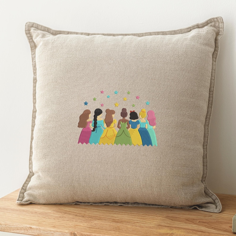May include: Beige square throw pillow with embroidered design. The design features eight figures in colorful gowns with various hairstyles, under a scattering of colorful stars. The pillow has a light brown border.