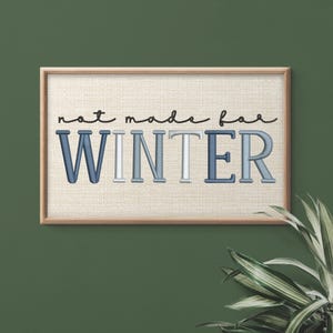 Puede incluir: Una obra de arte enmarcada con la frase "not made for WINTER". El texto est&aacute; en una mezcla de colores azul y blanco, con una fuente cursiva para "not made for" y una fuente de bloque para "WINTER". El fondo es de tela beige claro.