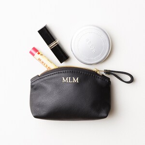 Small monogrammed leather clutch with makeup protruding out of clutch.