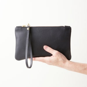 Hand holding black leather zipper clutch.