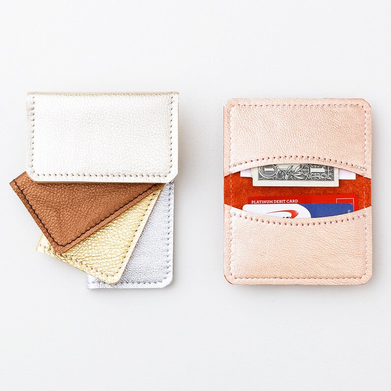 Set of five metallic leather credit card wallets in a variety of colors with metallic rose gold wallet open with credit cards and cash inside.