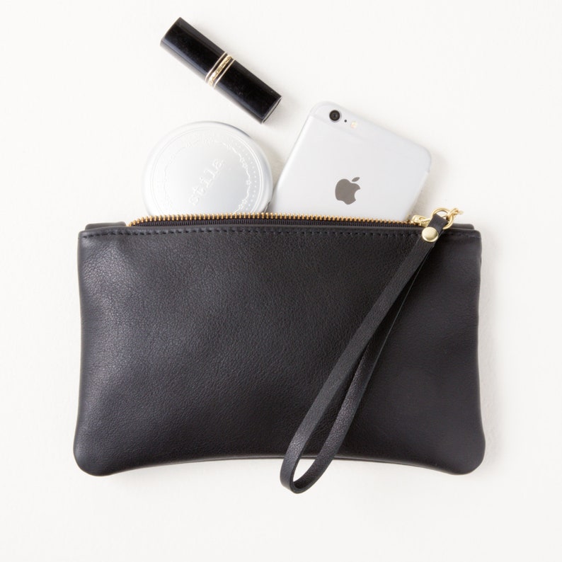 Black leather zipper clutch with wrist strap top view with cell phone and makeup partially inside clutch.