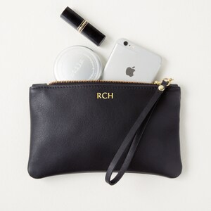 Monogrammed leather clutch with wrist strap top view with cell phone and makeup partially inside clutch.