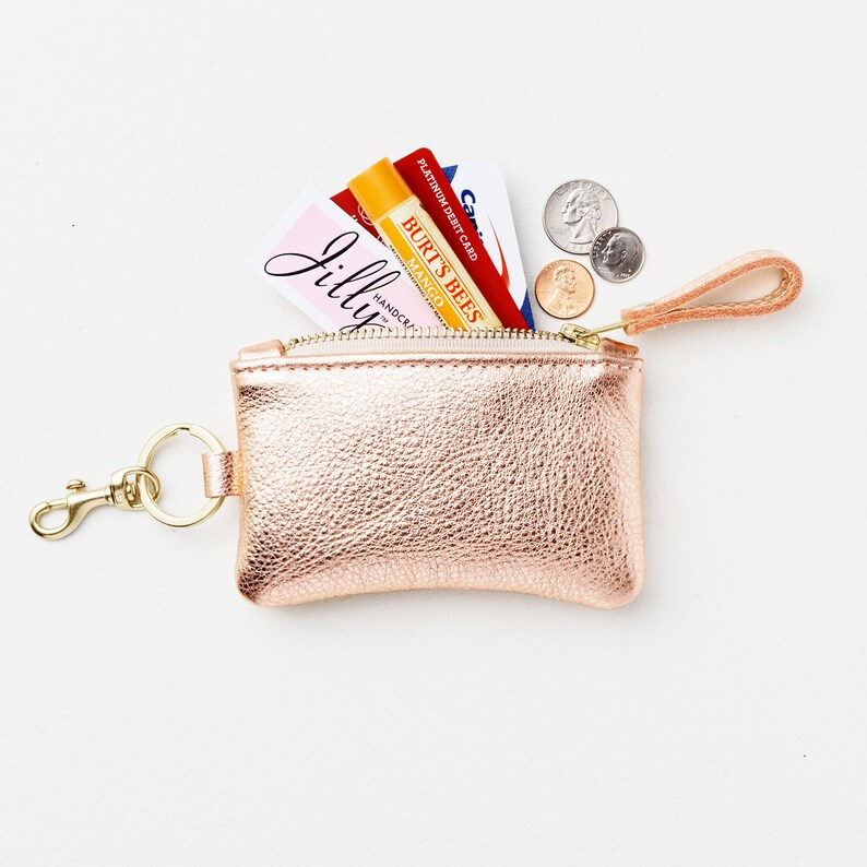 Metallic leather keychain zip wallet with credit cards, cash, business card, coins and lip balm protruding out of keychain wallet.