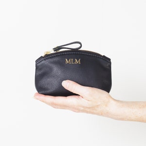 Hand holding small monogrammed leather clutch.