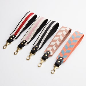 May include: Five colorful woven straps with black leather accents and gold metal clasps. The straps have different patterns, including red and white stripes, pink and white stripes, black and white stripes, pink and white chevron, and blue and white chevron.