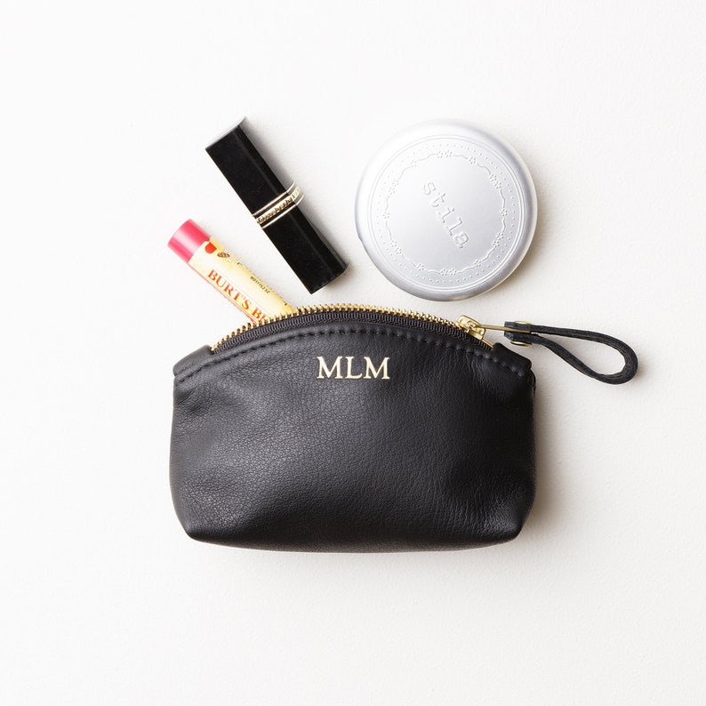 Small monogrammed leather clutch with makeup protruding out of clutch.