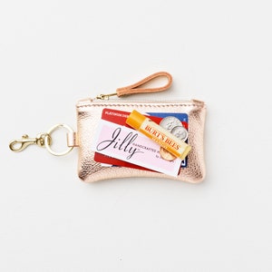 Metallic leather keychain zip wallet with credit cards, cash, business card, coins and lip balm placed on top of of keychain wallet for size reference.