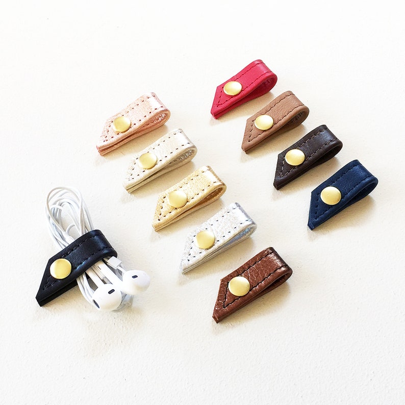 Set of ten leather cord keepers with button snap closures in a variety of colors with black cord keeper holding earbuds.