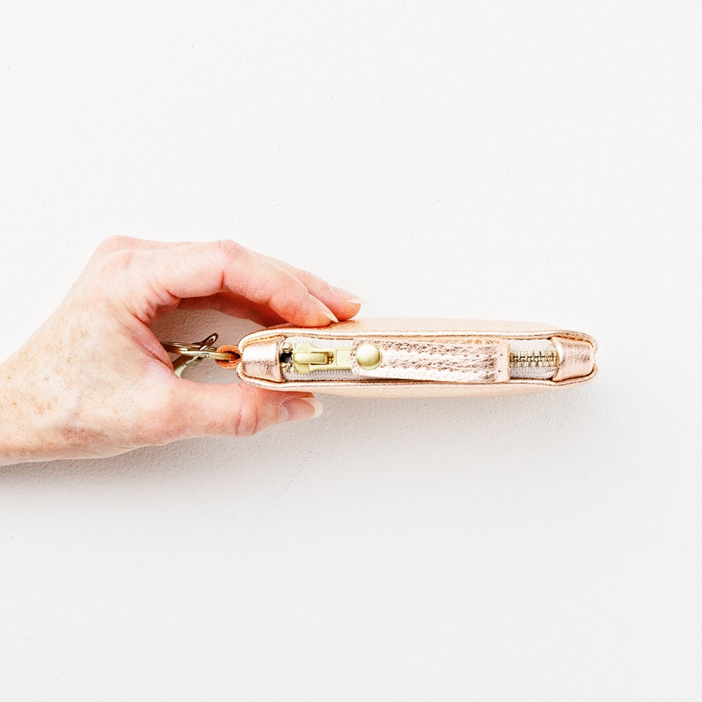 Hand holding metallic leather keychain zip wallet to show view of top zipper with matching leather zipper pull.