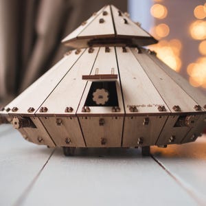 May include: A wooden model of Leonardo da Vinci's tank, featuring a conical shape with a rotating turret and wheels. The model is made of light-colored wood with dark brown accents. The text "Leonardo da Vinci" is visible on the side.