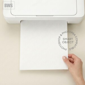 Può includere: Una stampante bianca stampa un foglio di carta bianco. Il foglio è tenuto da una mano. La carta ha le parole "PHOTOSHOP & PHOTOPAE COMPATIBLE SMART OBJECT" stampate.