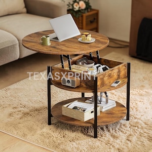 May include: A lift-top coffee table with a round, distressed wood surface. The table has a lower shelf and a hidden storage compartment. The table is supported by black metal legs. A laptop, mug, and snacks are on the table.