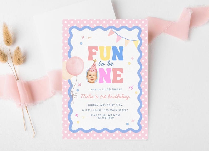 Może przedstawiać: R&oacute;żowe i niebieskie zaproszenie urodzinowe z napisem "FUN to be ONE". Zaproszenie zawiera zdjęcie dziecka w czapeczce urodzinowej, r&oacute;żowy balon i napis "Mila's 1st birthday".
