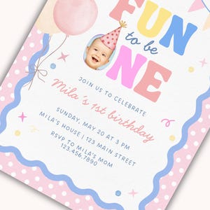 Może przedstawiać: Pastelowe zaproszenie urodzinowe z napisem "FUN to be ONE". Zaproszenie zawiera zdjęcie dziecka w czapeczce urodzinowej, balony i dekoracyjne obramowania. Na zaproszeniu widnieje napis "Mila's 1st birthday."