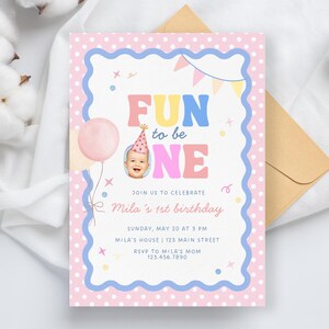 Może przedstawiać: Pastelowe r&oacute;żowe i niebieskie zaproszenie urodzinowe z napisem "FUN to be ONE". Zaproszenie zawiera zdjęcie dziecka w czapeczce urodzinowej, r&oacute;żowy balon i elementy dekoracyjne. Zaproszenie jest na 1. urodziny Mili.