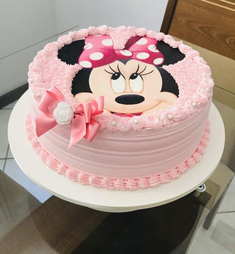 Pode incluir: Um bolo rosa e branco decorado com uma imagem da Minnie Mouse. O bolo tem um la&ccedil;o rosa e detalhes de p&eacute;rolas brancas.