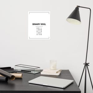 May include: A rectangular white wall poster featuring the black text BINARY SOUL centered at the top, followed by a horizontal line and five rows of binary code digits consisting of zeros and ones, all enclosed within a thin black rectangular border.