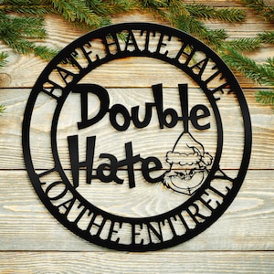 May include: A black metal sign with the words "HATE HATE HATE" around the outer circle and "Double Hate" in the centre. The sign also features a cartoon character wearing a Santa hat and the words "THE ENTIRELY" around the bottom.