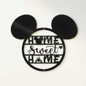 Puede incluir: Decoración de pared de metal negro en forma de orejas de Mickey Mouse con un círculo en el medio. El círculo tiene el texto "Home Sweet Home" con un pequeño corazón y una silueta del Castillo de Cenicienta.