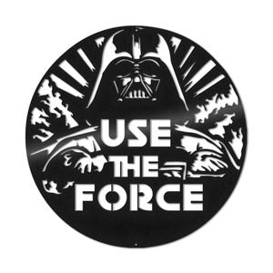 May include: Black and white metal wall art featuring Darth Vader from Star Wars. The art has a circular shape and the text "USE THE FORCE" is written below Darth Vader.