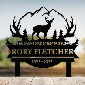 Könnte beinhalten: Schwarzes Metall-Gedenkschild mit einer Hirschsilhouette, Bergen und Bäumen. Auf dem Schild steht "IN LOVING MEMORY OF RORY FLETCHER 1975-2025". Das Design umfasst dekorative Geweihe und eine stilisierte Bergkette.